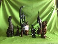 Full group of nine assorted wooden figurines and sculptures on green fabric background, showing range of sizes and shapes