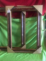 Pair of large gallery frames displayed against a green and red backdrop, with cardboard corner guards protecting the frames.