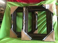 Pair of two gallery wood frames leaning against a green backdrop, showing full view including protective corner covers.