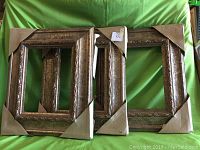 Three wooden frames overlapping and wrapped in protective cardboard on the corners, displayed on a green background