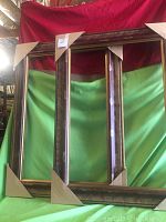 Two rectangular wooden mirrors standing side by side with adorned edges and cardboard corner protectors.