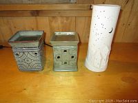 Photo showing two square ceramic Scentsy warmers and a tall white candle lantern on a wooden surface
