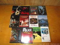 Photo showing 11 DVD and VHS cases arranged on a wooden surface including concert DVDs by Queen, Nirvana, Police, Jeff Buckley and instructional guitar DVD.