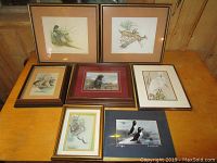 Eight framed wildlife prints and photo arranged on table showing subjects including pheasants, deer, dog, goose, owls, and puffins.