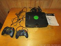 Full view of Xbox console, two wired controllers and instruction manual on wood surface