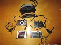 Photo of two portable cassette players, a Pentax film camera with soft black case, headphones and mounting strap on wooden surface