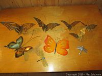 Top view of all nine items spread on wooden surface showing butterflies and dragonflies in metal/brass and orange painted finishes