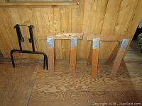 Three small wooden saw horses and black metal folding table legs on a wood floor in front of a wooden wall.