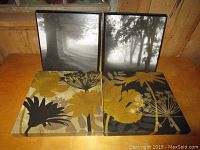 Four canvas wall prints arranged on a wooden surface: two black and white tree prints and two yellow and black floral prints.