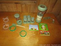 Full lot arranged on wooden surface including Baby Bullet blender, storage cups, lids, rings, spatula, and recipe books.