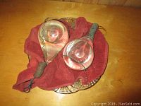 Photo showing two vintage glass fire extinguishers placed on a red cloth on a wooden table.