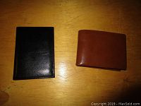 Photo of two wallets side by side on a wooden surface, one black and one brown, showing their overall size and leather texture.
