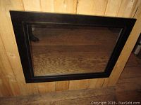 Mirror lying on a wood floor, showing the full black frame and glass reflecting the floor and wall.