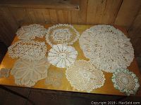All 10 vintage crochet and lace doilies laid out on wooden table displaying variety of patterns and sizes.
