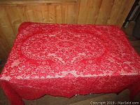 Red lace detailed tablecloth spread over a rectangular table showing intricate floral pattern and vintage style.