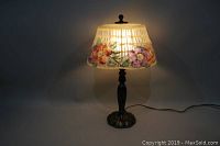 Lit front view showing painted floral glass shade and metal base