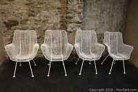 Front view of all four white painted wrought iron mesh chairs against stone wall