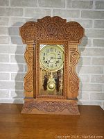 Front view of the complete antique mechanical clock showing the carved oak wooden case and glass front panel with decorative etching.