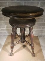 Front view of antique wooden piano stool with round adjustable seat and eagle claw feet.