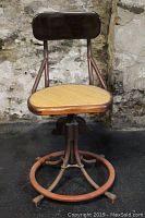 Front view of vintage industrial work stool showing cane seat, wooden backrest and metal frame with circular footrest.