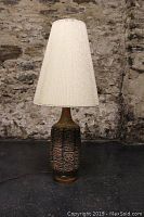 Front view of the lamp showing ceramic base with embossed geometric patterns and textured beige lampshade.