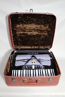 Accordion nestled in open red vinyl case showing interior plush lining and metal latches