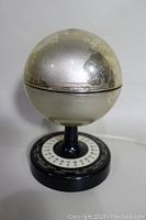 Full view of the globe lamp showing metallic globe with some peeling finish on top and black base.