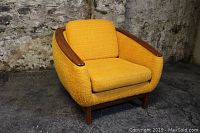 Front left angled view showing overall shape, teak armrests, cushion and upholstery.