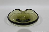 Front view of green and black Holmegaard art glass dish showing the central depression and curved edges.