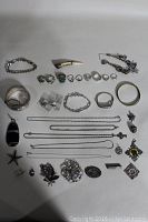 Overview of sterling silver jewelry lot showing rings, bracelets, necklaces, brooches, and pendants on white background.