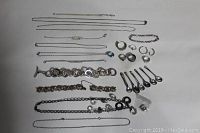 Lot of sterling silver jewelry displayed on white background showing multiple chains, bracelets, rings, hoop earrings, and six small spoons.