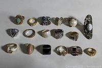 Overall view of 17 assorted rings laid out in rows on neutral surface