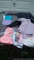 View showing assortment of toddler girls clothing including coats and shirts in various colors and styles spread on a surface outdoors.