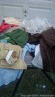 Overhead photo showing assorted womens plus size clothing including beige pants, green shirt/pant, striped blue and white item, brown garment, and white sheer sleepwear.