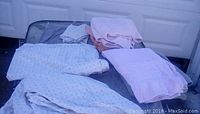 Photo shows folded queen bedding items including cover, sheet, and pillowcases beside folded towels in light and pastel colors on a black surface.