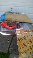 Folded Coleman cabin style tent in tan and blue with metal poles and stakes on a table.