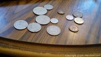 Photo showing twelve foreign coins arranged on wooden surface, varying sizes and designs.