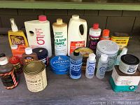 Photo of various plastic bottles and metal tins of cleaning and polishing products arranged on a wooden surface showing labels and container types.
