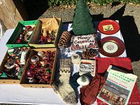 Full overview of Christmas decorations including ornaments in boxes, green metal tree, plaques, plates, knit socks, and holiday textiles