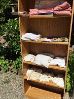 Photo showing multiple folded table cloths, napkins, and linens arranged on wood shelves outdoors
