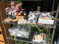 Wide view of metal shelves filled with bags and boxes containing sewing and crafting materials including yarns, ribbons, threads, and needles.