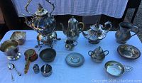 Photo showing a wide view of the assortment of pewter and silver plated serving dinnerware items arranged on a white cloth.