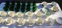 Entire lot spread out of coffee mugs, tea cups with saucers, showing grouping of green glass coffee mugs, white porcelain tea cups and saucers including multiple brands.