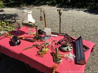 Multiple assorted lighting fixtures and lamps arranged on a red tablecloth outdoors, including traditional lamps with brass features and fabric shade, and glass accent pieces.