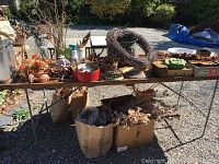 Wide view of table showing variety of dried flowers, wreath, floral sponges, marble bases, metal containers and pottery items arranged on and underneath the table.