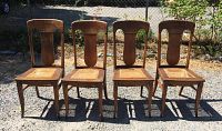 Four dark wooden chairs with vertical slat backs, arranged outdoors on gravel, showing overall condition and design.