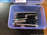 Clear plastic container holding a mix of vintage mechanical pencils and pens mainly black with metallic accents