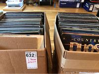 Two cardboard boxes filled with vinyl record albums, viewed from above, showing the spines and top edges of various albums.