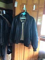 Front view of black leather bomber jacket on hanger showing leather exterior, flap pockets, collar and rib-knit hem and cuffs