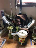 Overview of fishing gear including rods, waders, lantern, cooler, and stove grouped together indoors.